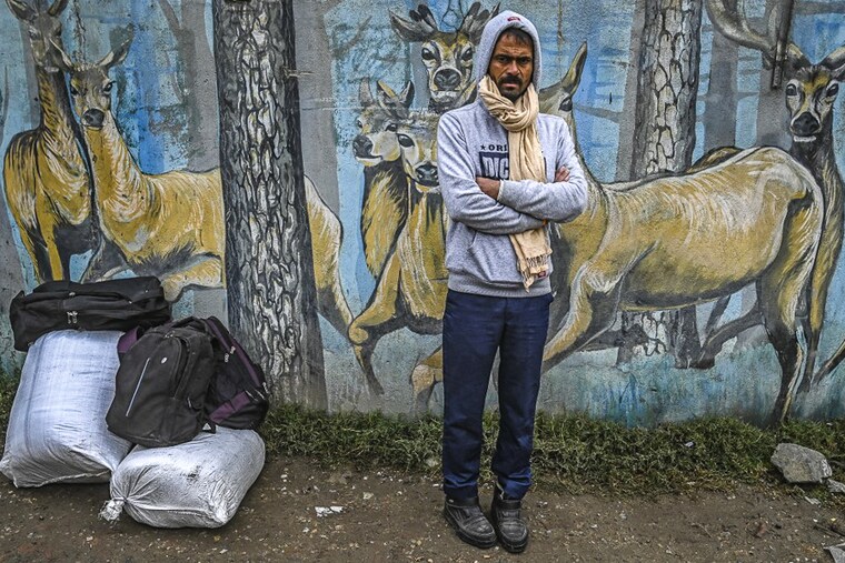 An Indian migrant worker awaits by a wall mural in Srinagar, Kashmir, to board a bus to return to his native home state, on October 19, 2021. Hundreds of labourers who are in Kashmir on work started fleeing the region following attacks on migrant labourers by suspected militants since early this week.