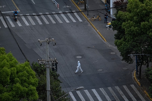 A worker wearing personal protective equipment (PPE) walks on a street during a COVID-19 lockdown in the Jing"an district in Shanghai on April 12, 2022. (Credit: Hector RETAMAL / AFP)