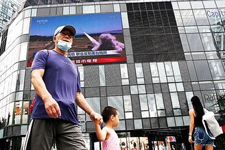 People walk in front of a large screen showing a news broadcast about China"s military exercises encircling Taiwan, in Beijing on August 4, 2022. China"s largest-ever military exercises encircling Taiwan kicked off on August 4, in a show of force straddling vital international shipping lanes after a visit to the island by US House Speaker Nancy Pelosi.