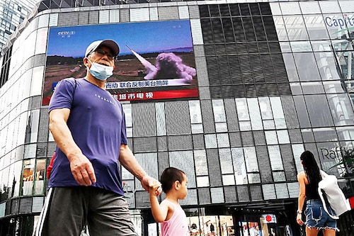 People walk in front of a large screen showing a news broadcast about China"s military exercises encircling Taiwan, in Beijing on August 4, 2022. China"s largest-ever military exercises encircling Taiwan kicked off on August 4, in a show of force straddling vital international shipping lanes after a visit to the island by US House Speaker Nancy Pelosi.