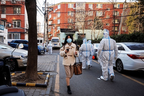 A woman walks past pandemic prevention workers in a neighbourhood where residents do home quarantine, as coronavirus disease (COVID-19) outbreaks continue in Beijing, December 8, 2022.