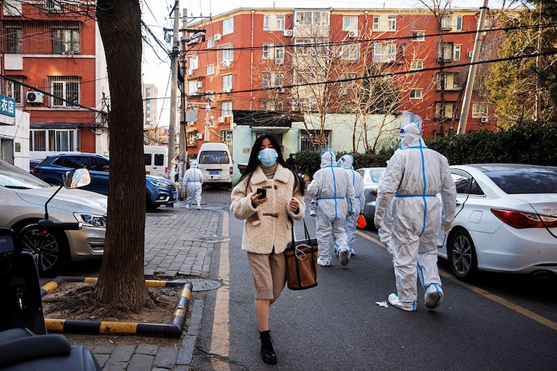 A woman walks past pandemic prevention workers in a neighbourhood where residents do home quarantine, as coronavirus disease (COVID-19) outbreaks continue in Beijing, December 8, 2022.