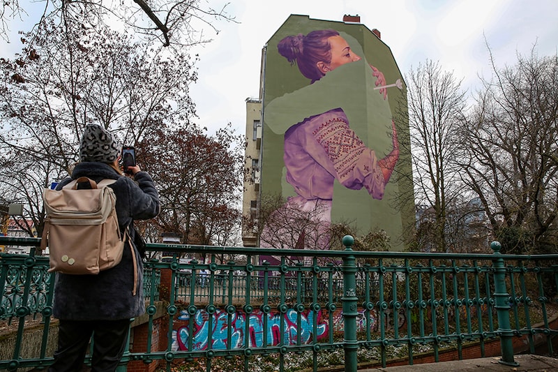 A Ukrainian woman takes a photo of a mural by the innerfields art collective titled "Absent," depicting a Ukrainian woman who lost a loved one to war, on December 16, 2022, in Berlin, Germany. Tens of thousands of Ukrainians are estimated to have been killed since Russia launched its large-scale invasion on February 24, but an official civilian or military death toll has not been given. Image: Adam Berry/Getty Images