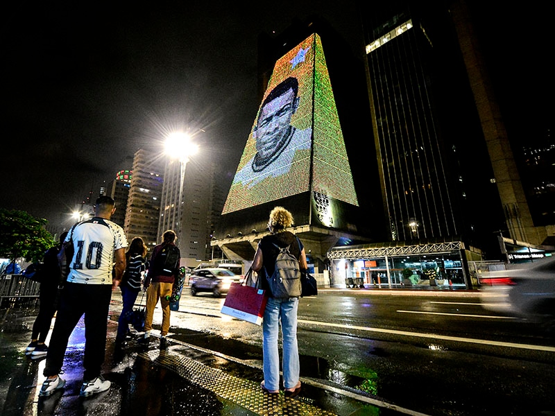 People stand in front of a building where an image of football icon Pele is displayed on a building as a tribute after his passing on December 29, 2022 in Sao Paulo, Brazil. Brazilian football icon Edson Arantes do Nascimento, better known as Pele, died on December 29, 2022, aged 82, after a battle with cancer. The three-time World Cup champion with Brazil is considered one of the greatest football legends of all time.