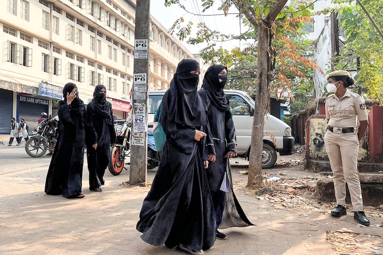 Hijab wearing schoolgirls arrive to attend their classes as a policewoman stands guard outside a government girls school in Udupi, Karnataka, India, February 16, 2022. Schools reopened in southern India under tight security after authorities banned public gatherings following protests over Muslim girls wearing the hijab in classrooms.
