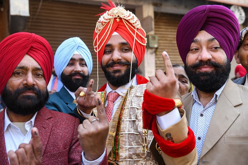 A newly married groom (C) shows his inked finger after casting his ballot at a polling station in a village on the outskirts of Amritsar on February 20, 2022, during the Punjab state assembly elections.