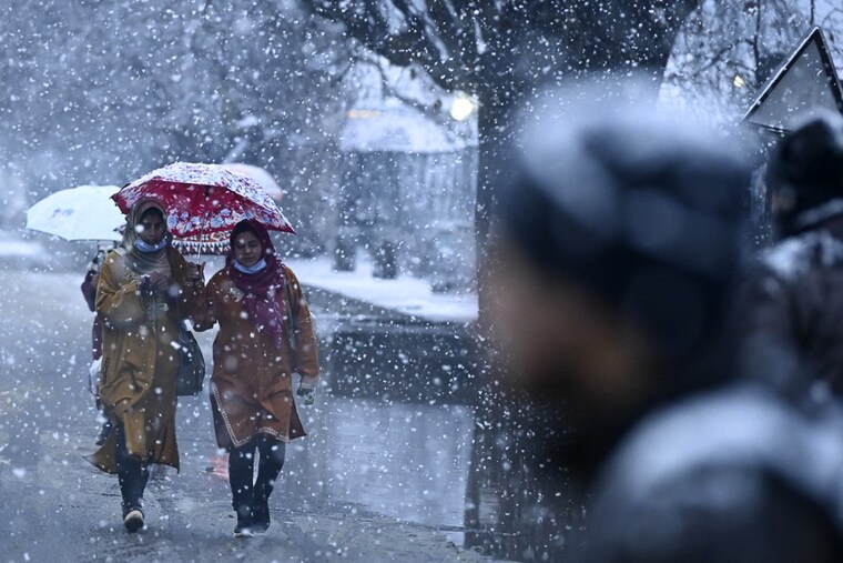 People walk along a street as snowfall envelops Srinagar on January 7, 2022. The snowfall forced cancellation of several flights to Srinagar airport.