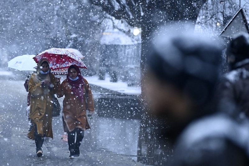 People walk along a street as snowfall envelops Srinagar on January 7, 2022. The snowfall forced cancellation of several flights to Srinagar airport.