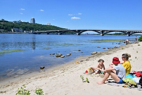 A family sits on the sandy shores of the Dnipro river that runs through the Ukrainian capital of Kyiv on July 2, 2022. Ivan Sukhanov and his family used to holiday by the Black Sea. This summer they are gong no further than the banks of the Dnipro river in the heart of Kyiv. Four months after Russian troops marched into Ukraine in February "we"re getting used to it," says the electrical engineer. (Photo by Sergei SUPINSKY / AFP)â€‹