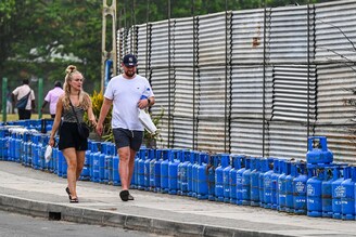 Tourists walk past liquefied petroleum gas (LPG) cylinders placed by people queueing to buy fuel in Galle, Sri Lanka on July 4, 2022. Sri Lanka depends on imports for most of its needs and owes about $800 million to seven fuel suppliers to date.