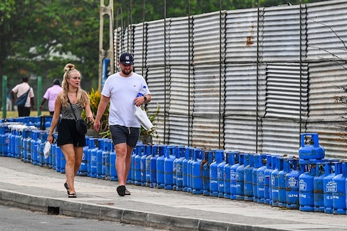 Tourists walk past liquefied petroleum gas (LPG) cylinders placed by people queueing to buy fuel in Galle, Sri Lanka on July 4, 2022. Sri Lanka depends on imports for most of its needs and owes about $800 million to seven fuel suppliers to date.