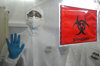 A technician wearing personal protective equipment (PPE) gestures next to a biohazard sign inside a molecular laboratory facility set up to test for the monkeypox disease. The lab is inaugurated at the King Institute in Chennai, on July 28, 2022.