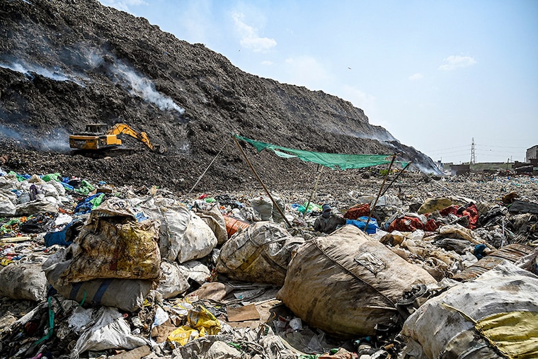 A man segregates plastic, polythene, and other reusable materials from waste collected by ragpickers as smoke billows during an ongoing fire at Bhlaswa landfill seen in the background in New Delhi on June 4, 2022.