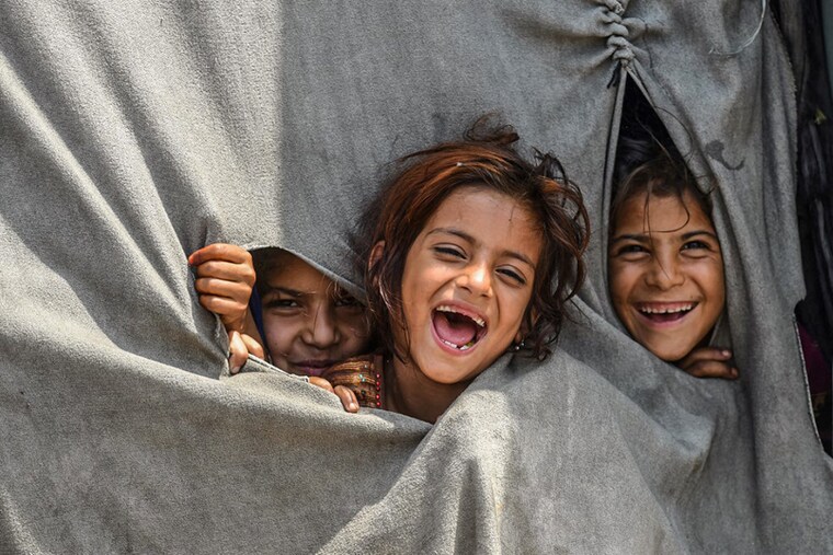 Children of Afghan refugees living in Pakistan react to the camera from inside their makeshift tent on the outskirts of Lahore on June 19, 2022, on the eve of World Refugee Day.