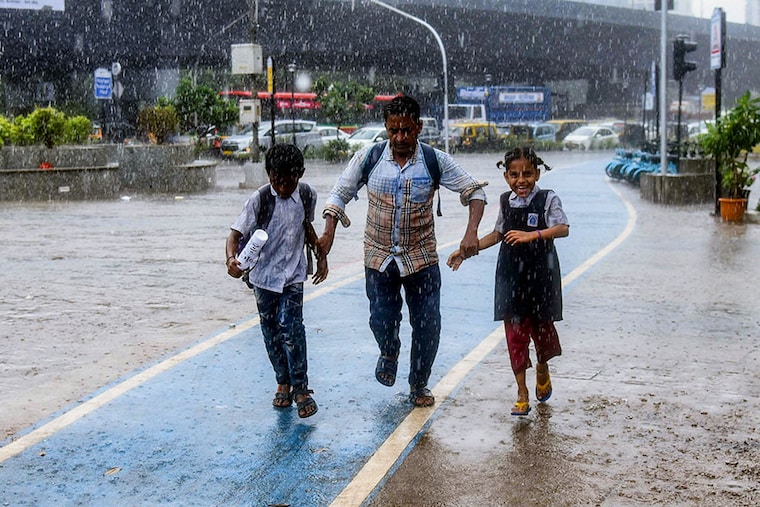 Two school children run with their father for cover from heavy rains near Kalanagar in Bandra on June 29, 2022.