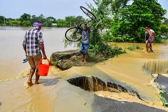 A man carrying his bicycle crosses a damaged road due to flooding after heavy rains in Nagaon, Assam, on May 19, 2022. At least 10 people, including a four-year-old child, have died in floods and landslides this week after unusually heavy rains pummelled several parts of India, as forecasters warned on May 18 of more deluges.