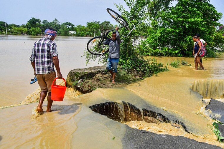 A man carrying his bicycle crosses a damaged road due to flooding after heavy rains in Nagaon, Assam, on May 19, 2022. At least 10 people, including a four-year-old child, have died in floods and landslides this week after unusually heavy rains pummelled several parts of India, as forecasters warned on May 18 of more deluges.