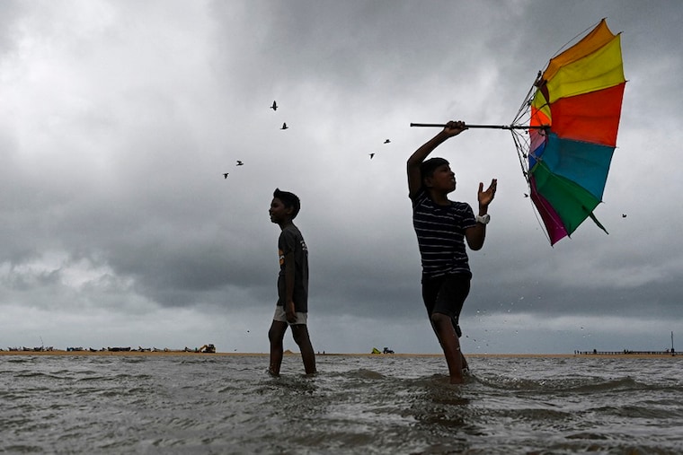 Boys walk with an umbrella amid gusty winds as dark clouds loom over the Marina beach in Chennai on November 11, 2022.