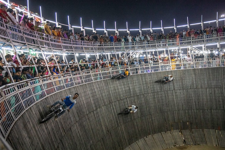 Stunt riders perform a daring show, biking on a vertical, makeshift wooden racetrack known as the "Well of Death" at a carnival in Noida, Uttar Pradesh, India on October 04, 2022. The "Well of Death", a popular draw for families at carnivals during holidays this festival season, attracting large numbers of people who buy tickets to watch them.