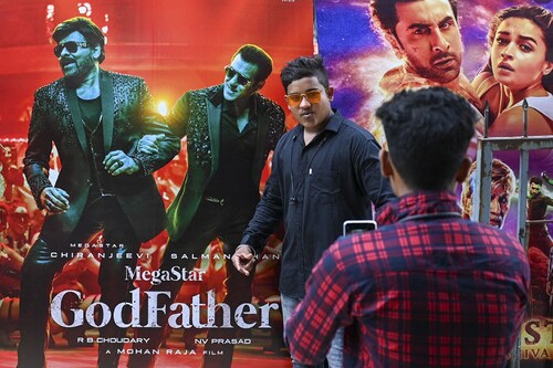 In this picture taken on October 1, 2022, a moviegoer poses for a picture next to a cinema poster of Tollywood star Chiranjeevi and Bollywood"s Salman Khan outside the G7 multiplex in Mumbai. India"s Bollywood film industry, long part of the cultural fabric of the movie-mad country of 1.4 billion people, is facing its biggest-ever crisis as streaming services and non-Hindi language rivals steal its sparkle. Image:&nbspPunit PARANJPE / AFP