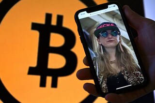 This illustration photo shows Heather Morgan, also known as "Razzlekhan," on a phone in front of the Bitcoin logo displayed on a screen, in Washington, DC, February 9, 2022. A couple accused of seeking to launder the bitcoin were arrested in New York, the department said. Ilya Lichtenstein, 34, and his wife Heather Morgan, 31. Image: Olivier DOULIERY / AFP