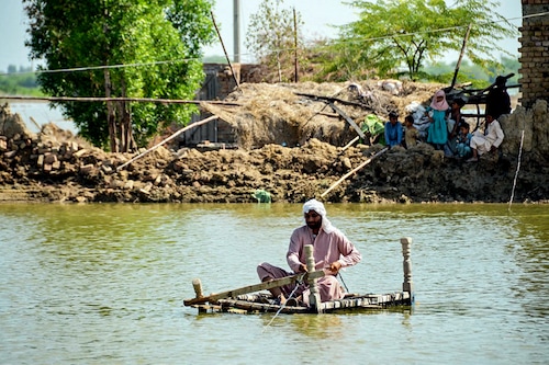 A flood-affected man uses a makeshift raft to cross s stream of flood waters near his damaged house in Jaffarabad, Balochistan province on September 23, 2022. Image: Fida HUSSAIN / AFP