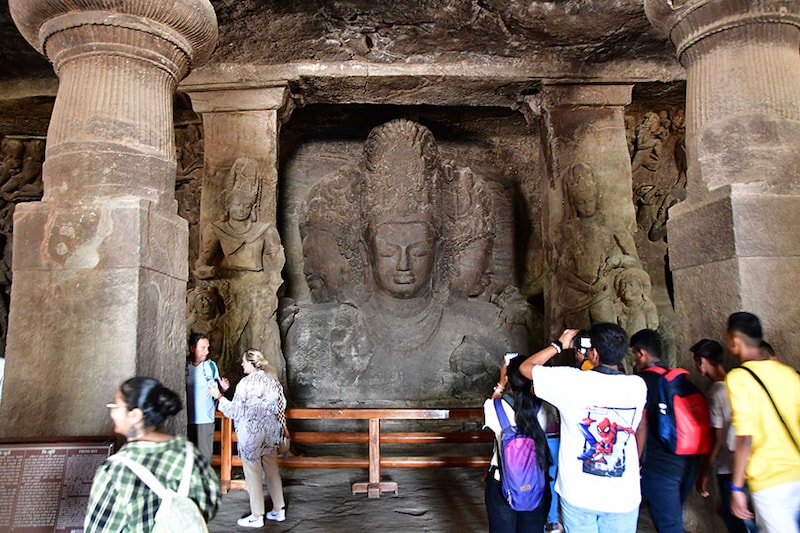 Tourists behold the spectacular rock sculpture of three-faced Shiva at Elephanta Caves, a UNESCO World Heritage Site off the Mumbai coast on World Heritage Day, April 18, 2023. The 1,300-year-old rock-cut temples were created in volcanic rock, using just a hammer and chisel.