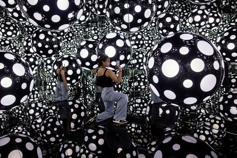 A woman takes photos at an art installation called Dots Obsession - Aspiring to Heaven’s Love by artist Yayoi Kusama’s with her signature polka dots and reflective mirrors in Hong Kong on August 4, 2023.