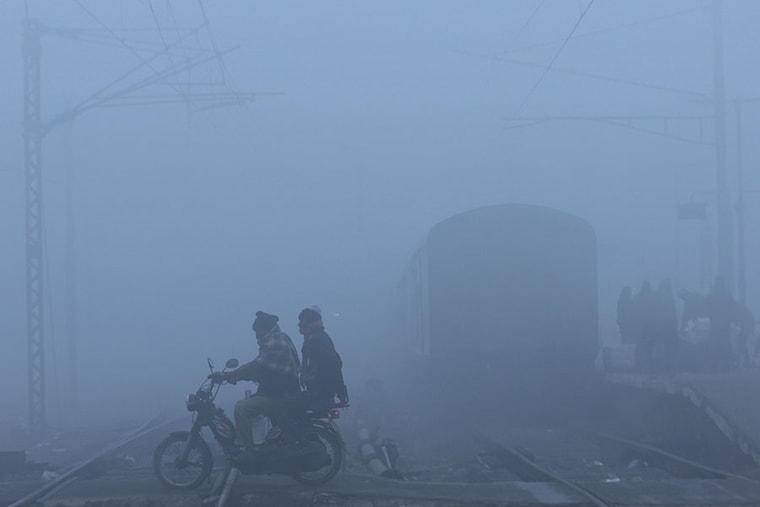 Men on a motorbike cross railway tracks amidst an intense fog on a cold winter morning in New Delhi, India, January 9, 2023. With the minimum temperature falling below 2 degrees celsius and visibility under 200m, over 100 flights were delayed and 42 trains were running late in the capital as the cold wave caused city schools to remain shut until mid-January