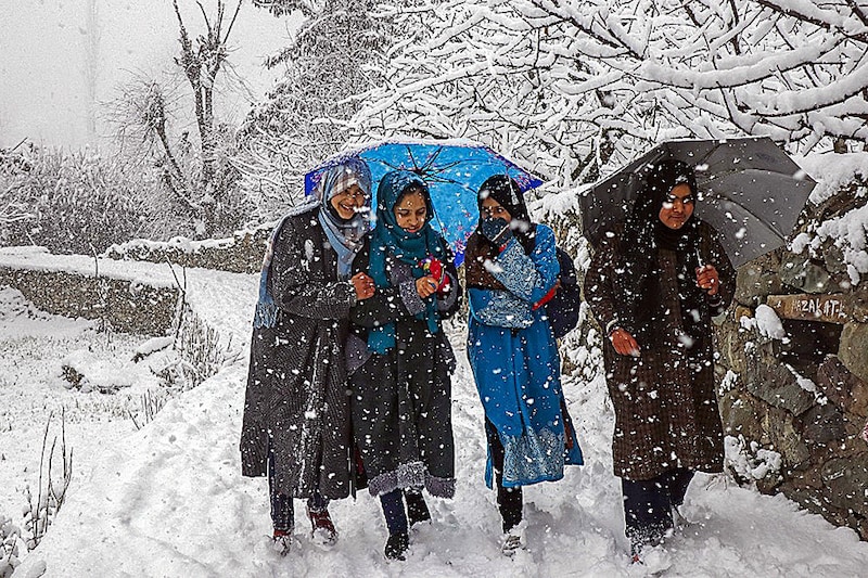 A group of girls walk along a path during a snowfall on the outskirts of Srinagar on January 13, 2023.