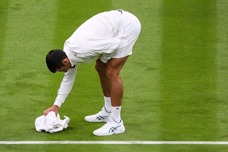 Serbia"s Novak Djokovic jokes as he attempts to dry the grass of Center Court with a towel as the rains start to fall during his men"s singles tennis match against Argentina"s Pedro Cachin on the first day of the 2023 Wimbledon Championships at The All England Tennis Club in Wimbledon, southwest London, on July 3, 2023.