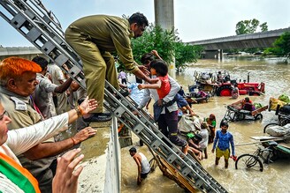 Delhi Fire Service personnel helping residents to climb on a flyover after being displaced by the rising water level of river Yamuna after heavy monsoon rains near Mayur Vihar Side on July 12, 2023, in New Delhi, India.