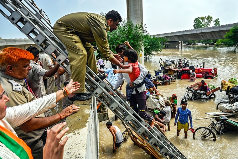 Delhi Fire Service personnel helping residents to climb on a flyover after being displaced by the rising water level of river Yamuna after heavy monsoon rains near Mayur Vihar Side on July 12, 2023, in New Delhi, India.