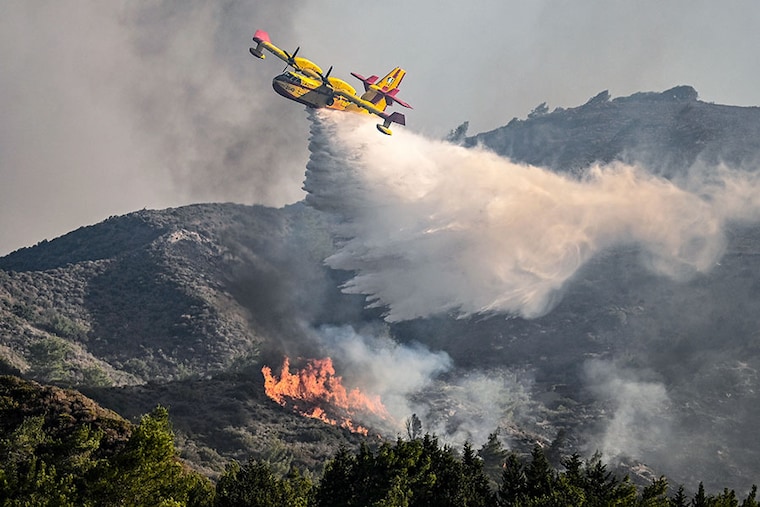 A firefighting aircraft drops water over a wildfire close to the village of Vati in the southern part of the Greek island of Rhodes, about 70 km southwest of the capital city, on July 25, 2023. Some 30,000 people fled the flames on Rhodes at the weekend, the country"s largest-ever wildfire evacuation as the prime minister warned that the heat-battered nation was "at war" with several wildfires and spoke of three difficult days ahead.