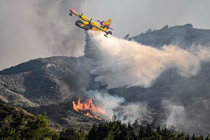 A firefighting aircraft drops water over a wildfire close to the village of Vati in the southern part of the Greek island of Rhodes, about 70 km southwest of the capital city, on July 25, 2023. Some 30,000 people fled the flames on Rhodes at the weekend, the country"s largest-ever wildfire evacuation as the prime minister warned that the heat-battered nation was "at war" with several wildfires and spoke of three difficult days ahead.