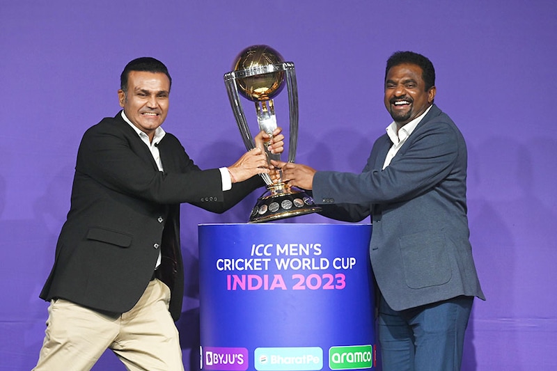 Former Indian cricketer Virender Sehwag jokes with former Sri Lankan cricketer Muttiah Muralitharan while posing with the trophy of the upcoming ICC Men"s Cricket World Cup during an event announcing the tournament"s schedule, in Mumbai on June 27, 2023. India will host Pakistan"s cricket team for the first time in seven years for the 50-over World Cup, the International Cricket Council said on June 27. The tournament will begin on October 5, with holders England taking on New Zealand at the world"s biggest cricket stadium in Ahmedabad, which will also host the final.