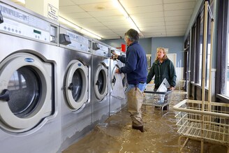 Patrick Cerruti and his wife Pamela take coins out of washing machines inside the flooded Pajaro Coin Laundry on March 14, 2023, in Pajaro, California. Northern California has been hit by another atmospheric river that has brought heavy rains and flooding throughout the region. The town has been inundated with floodwaters since Saturday after a levee was breached along the Pajaro River.