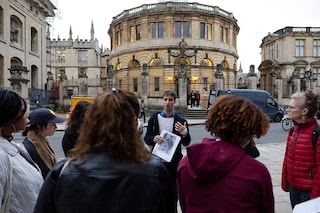 Tour guide Oliver talks with a group of people attending an "Uncomfortable Oxford" tour outside the Sheldonian Theatre on Broad Street, in Oxford. 
Image: Henry Nicholls / AFPÂ©