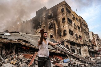 A man reacts outside a burning collapsed building following Israeli bombardment in Gaza City. Death toll in the latest strikes between Hamas and Israel has crossed over 1,400 in the Gaza Strip. The Israeli military confirmed it had hit several Hamas targets during the night in the Palestinian enclave on October 12.