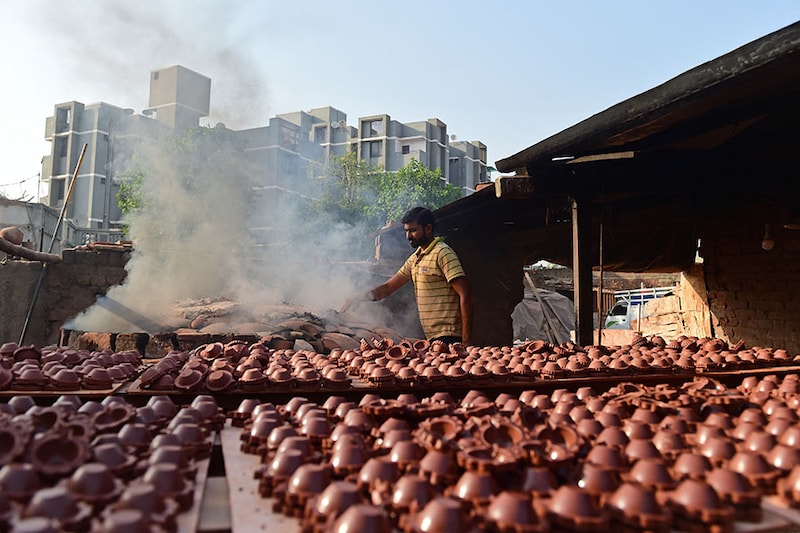 A potter works beside traditional earthen oil lamps kept in an oven ahead of Diwali on the outskirts of Ahmedabad, Gujarat on October 25, 2023.