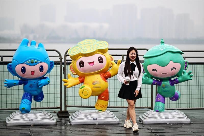 A woman poses for photographs with the 2023 Asian Games mascots (L-R) Chenchen, Congcong and Lianlian along the promenade of Qiantang River in Hangzhou in China"s eastern Zhejiang province on September 22, 2023.