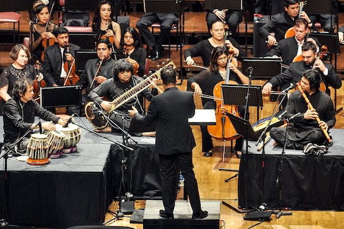 Zakir Hussain (on the tabla), Niladri Kumar (on the sitar), and Rakesh Chaurasia (on the flute) perform a triple concerto, composed by Hussain, along with the Symphony Orchestra of India led by conductor Alpesh Chauhan (standing) at the NCPA, Mumbai. The concerto will go on a three-city tour of the UK in November-December. Image: Courtesy NCPA