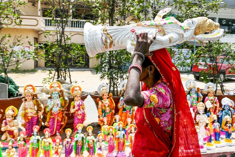 A vendor carries an idol of Lord Ram to arrange it along with other Hindu deities by the roadside in Hyderabad on April 16, 2024, on the eve of Ram Navami festival.