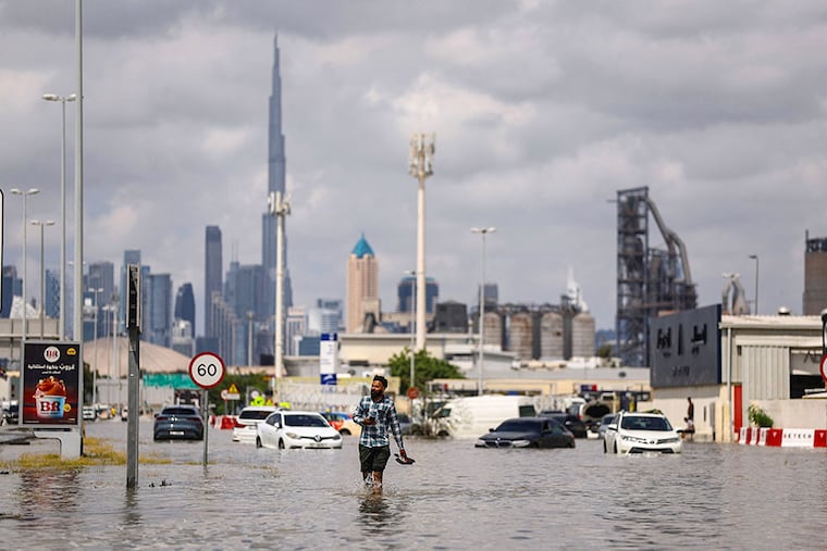 A person walks in flood water caused by heavy rains, with the Burj Khalifa tower visible in the background, in Dubai, United Arab Emirates, on April 17, 2024.