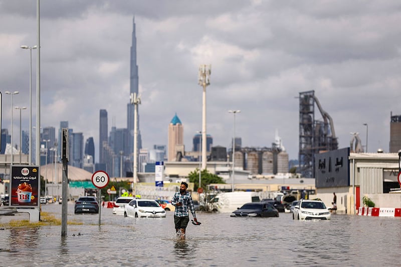A person walks in flood water caused by heavy rains, with the Burj Khalifa tower visible in the background, in Dubai, United Arab Emirates, on April 17, 2024.