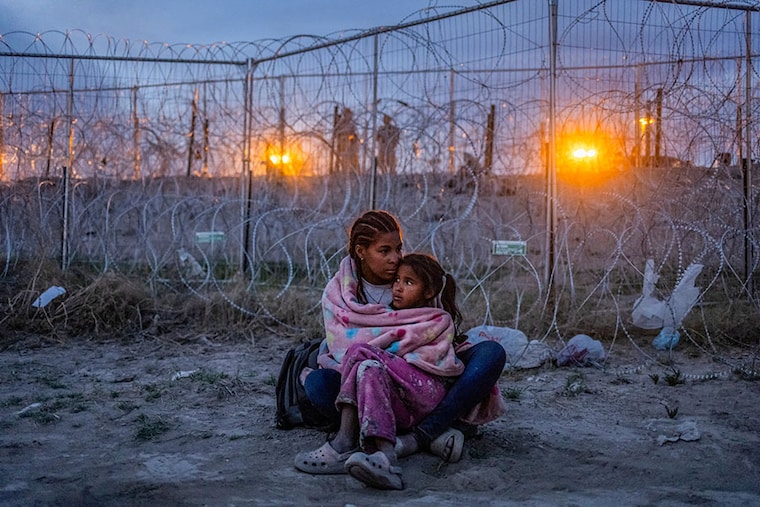 Army National Guard soldiers stand in the background as Michel, 26, of Venezuela, protects her seven-year-old daughter Aranza from Mexican immigration authorities patrolling near the dry riverbed of the Rio Grande as the migrants search for entry into the United States from the international boundary between Ciudad Juarez, Mexico and El Paso, Texas on April 24, 2024.