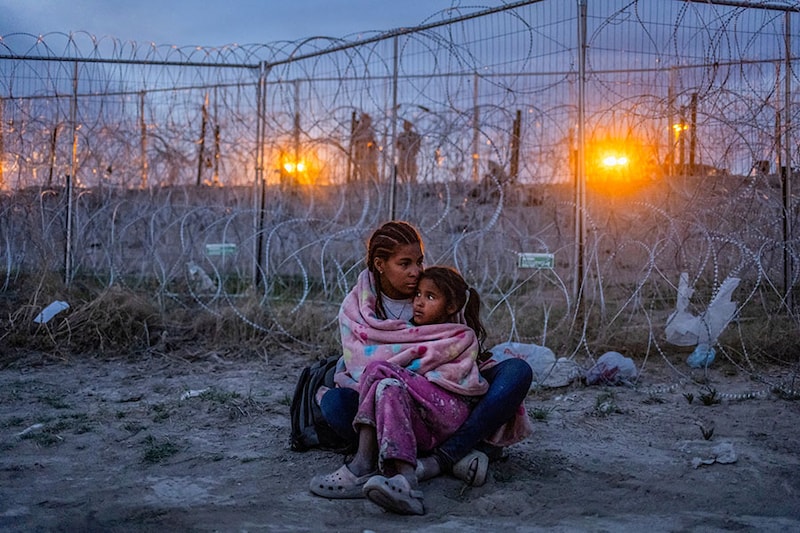 Army National Guard soldiers stand in the background as Michel, 26, of Venezuela, protects her seven-year-old daughter Aranza from Mexican immigration authorities patrolling near the dry riverbed of the Rio Grande as the migrants search for entry into the United States from the international boundary between Ciudad Juarez, Mexico and El Paso, Texas on April 24, 2024.