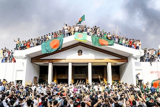 Anti-government protestors display Bangladesh"s national flag as they storm Prime Minister Sheikh Hasina"s palace in Dhaka on August 5, 2024. Bangladesh army chief Waker-Uz-Zaman spent nearly four decades rising to the top of the military and said on August 5 that he was "taking full responsibility" after Prime Minister Sheikh Hasina was ousted and fled.
