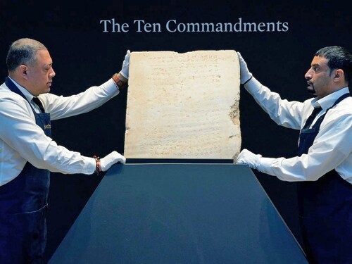 Sotheby’s workers hold one of the most widely known and influential texts in history: the oldest inscribed stone tablet of the Ten Commandments during a press preview at Sotheby’s in New York, on December 9, 2024. 
Image: Timothy A. Clary / AFPÂ©