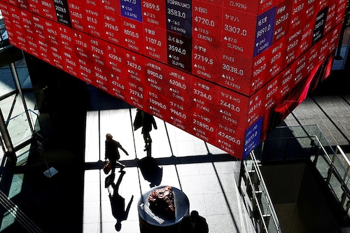 Visitors walk under Japan"s Nikkei stock prices quotation board inside a building in Tokyo on February 16, 2024. Japanese stock prices are within sight of a historic peak reached during the nation"s economic heyday in 1989 as global investors return in droves.
